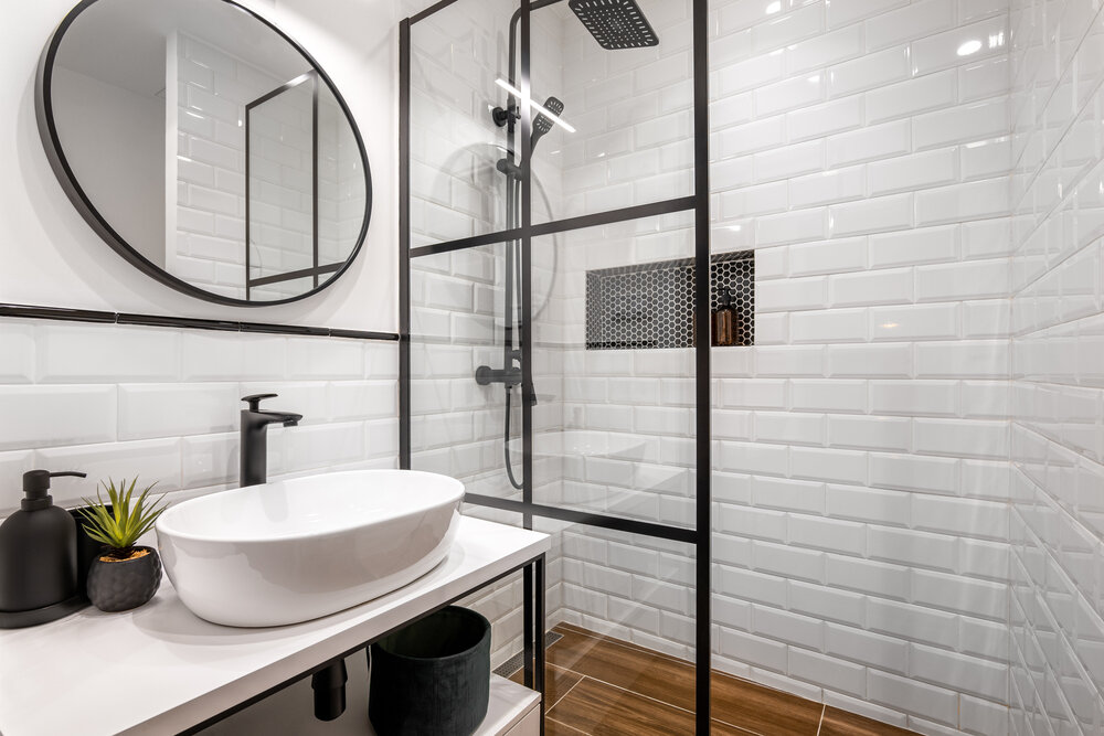 Jednoduchá koupelna s černou sprchou a kulatým zrcadlem 